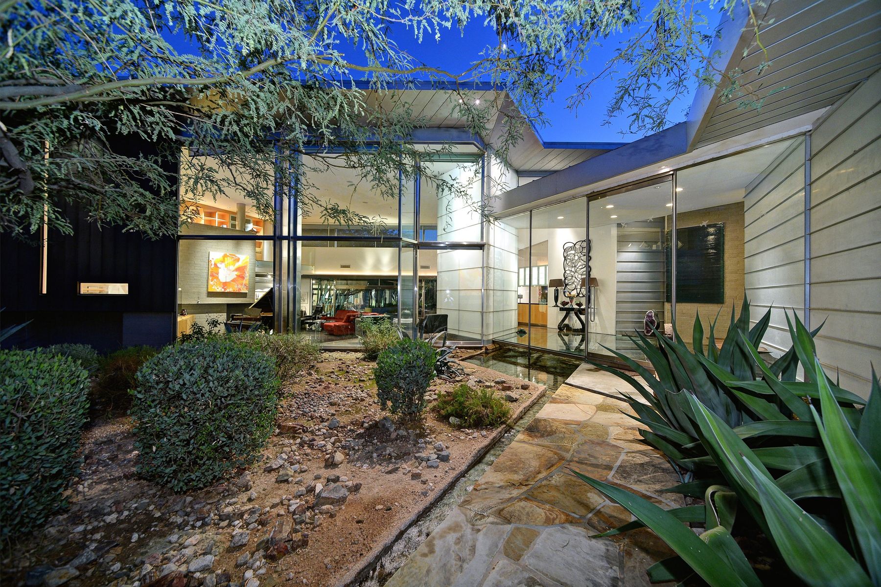 Contemporary glass home with a desert courtyard and water feature at dusk