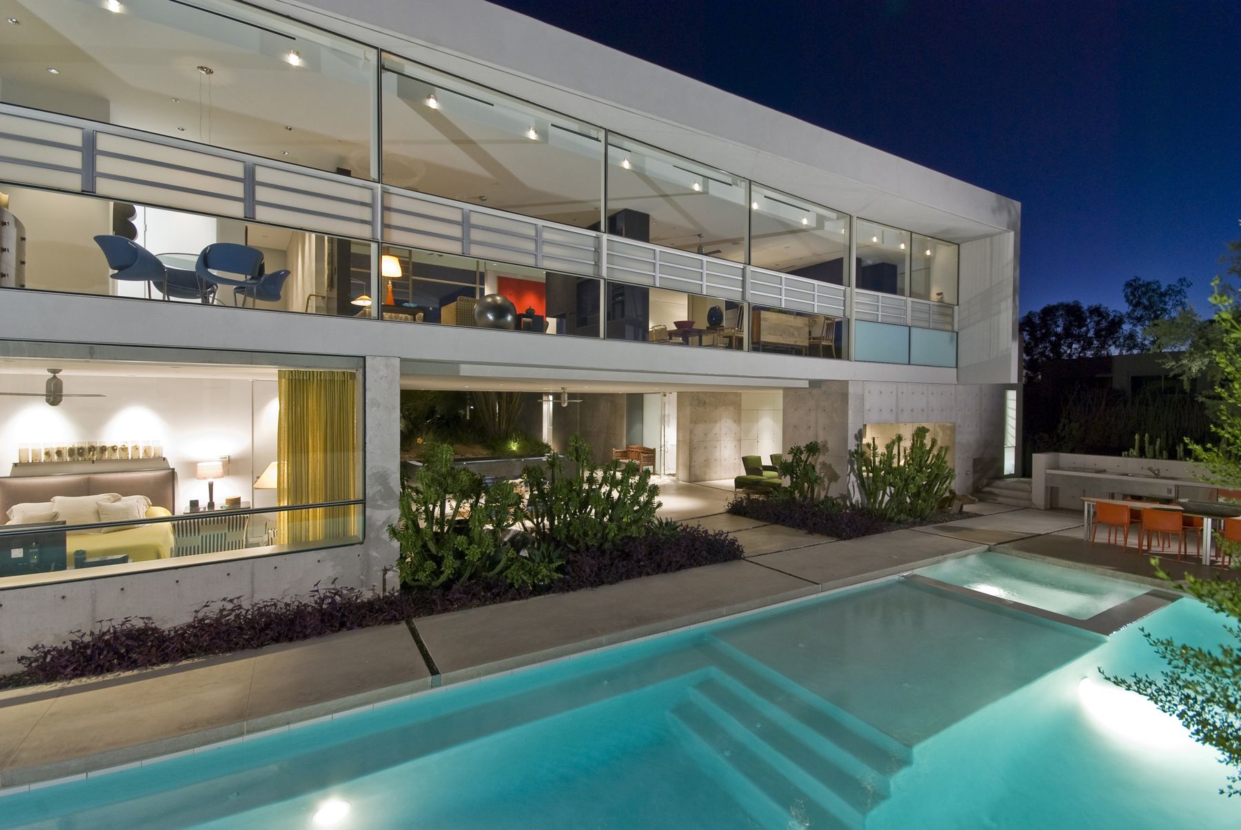 Two-story modern glass and concrete home with a lit pool at night